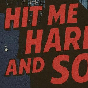 Pu&ograve; includere: Primo piano di un tessuto nero con le parole "HIT ME HARD AND SO" in grandi lettere rosse. Il testo ha un aspetto invecchiato e strutturato. Sul lato sinistro dell'immagine &egrave; visibile una grafica blu e bianca.