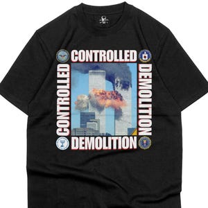 以下が含まれることがあります： 黒いTシャツ。世界貿易センタービルの炎と煙の画像と、白い文字で「CONTROLLED DEMOLITION」と書かれています。Tシャツは丸首で半袖です。