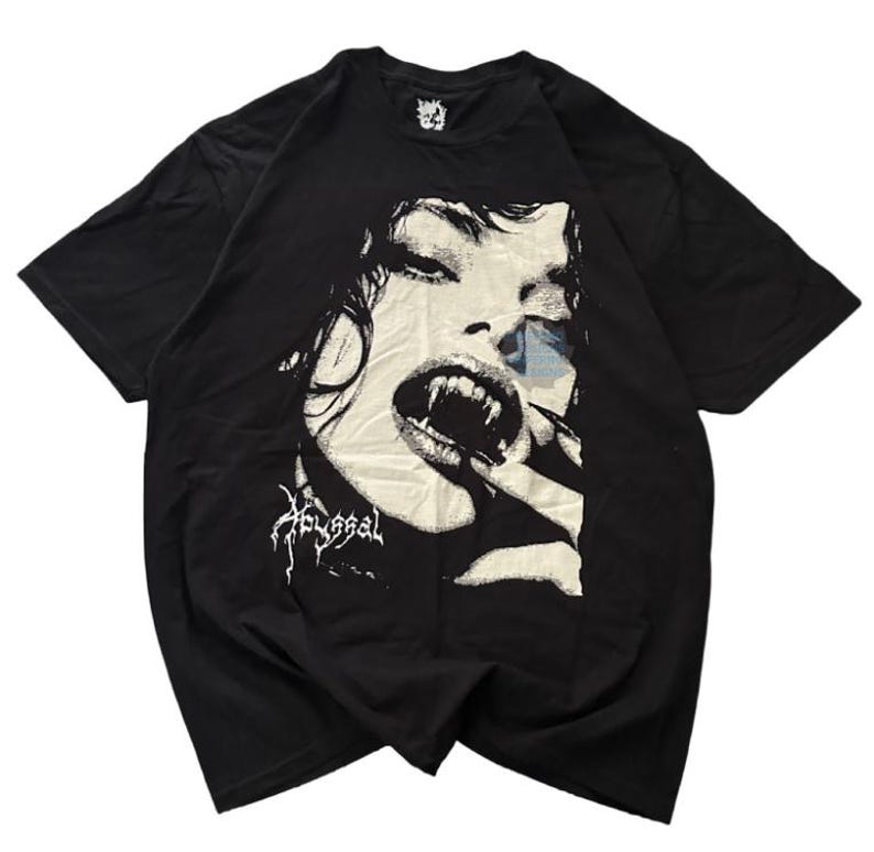 May include: Black t-shirt featuring a graphic of a woman with vampire fangs. The design is in black and white, with the word "Abyssal" in a stylized font below the image. The shirt has a crew neck and short sleeves.