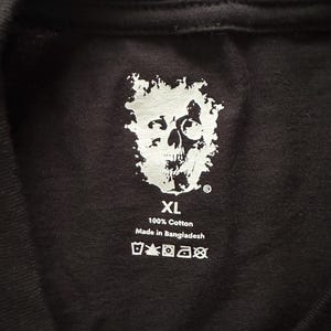 May include: Black XL t-shirt with a white skull graphic. The shirt is made of 100% cotton and includes care instructions. The text "Made in Bangladesh" is also visible.
