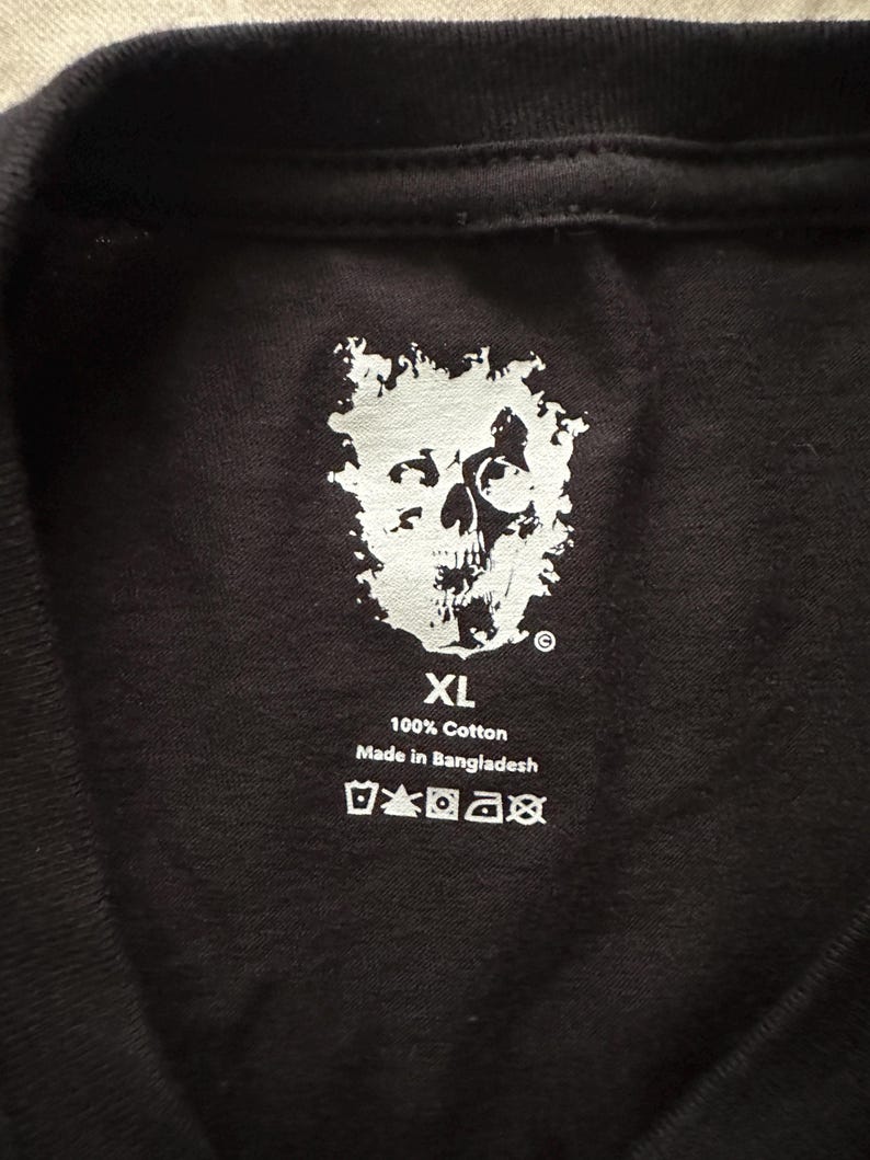May include: Black XL t-shirt with a white skull graphic. The shirt is made of 100% cotton and includes care instructions. The text "Made in Bangladesh" is also visible.