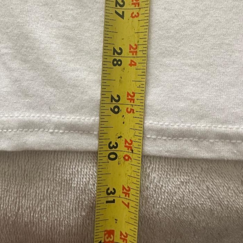 May include: A white fabric is measured with a yellow tape measure. The tape measure shows measurements from 27 to 31 inches. The fabric has a seam running horizontally across the middle.