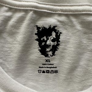 May include: White XL cotton t-shirt with a black skull graphic. The shirt is made of 100% cotton and is made in Bangladesh. The shirt has a crew neck and is suitable for casual wear.