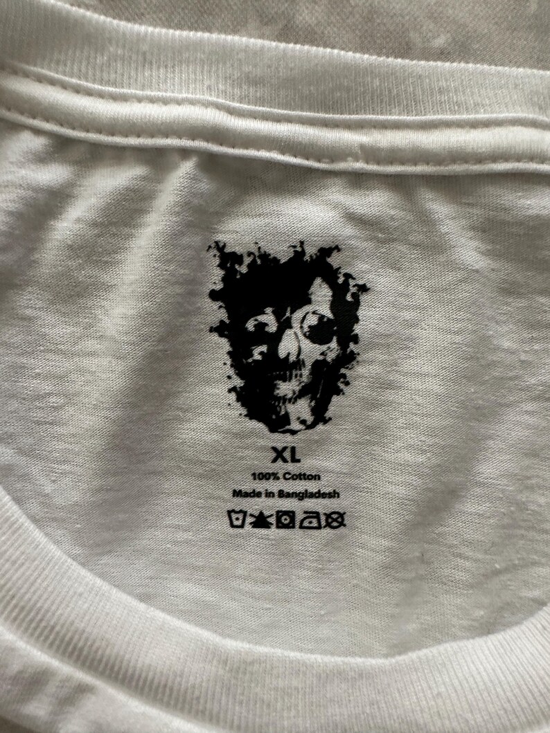 May include: White XL cotton t-shirt with a black skull graphic. The shirt is made of 100% cotton and is made in Bangladesh. The shirt has a crew neck and is suitable for casual wear.