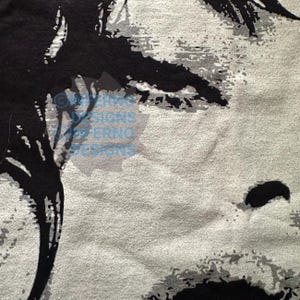 May include: Close-up of a textured fabric with a black and gray abstract design. The design features organic shapes and patterns against a light gray background. The fabric has a soft, slightly blurred appearance.