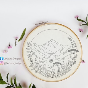 Könnte beinhalten: Ein Stickrahmen mit einem schwarz-weißen Berglandschaftsdesign. Das Kunstwerk zeigt eine Bergkette, einen See und florale Elemente. Der Rahmen ist aus Holz und der Stoff ist hellbeige. Der Text "Larisana Designs" ist sichtbar.