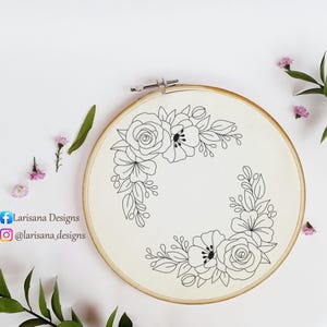 Könnte beinhalten: Ein Stickrahmen mit floralem Design. Das Design zeigt schwarze Linienzeichnungen von Blumen und Blättern, die in zwei Ecken auf einem cremefarbenen Stoff angeordnet sind. Der Holzrahmen ist mit einem Metallverschluss befestigt. Der Text "Larisana Designs" und Social-Media-Handles sind sichtbar.