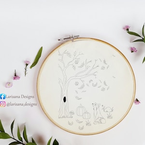 May include: A round wooden embroidery hoop containing white fabric with a black line art design of a tree with falling leaves, two pumpkins, and a fox. The text Larisana Designs and @larisana_designs is printed on the left side of the image.