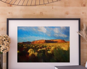 May include: A framed painting of a desert landscape with a red rock formation in the distance. The sky is blue with white clouds. The foreground is filled with green bushes.