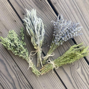 May include: Four bundles of dried herbs, including thyme, sage, lavender, and rosemary, are arranged on a weathered wooden surface. Each bundle is tied with twine, showcasing the natural textures and colors of the herbs.