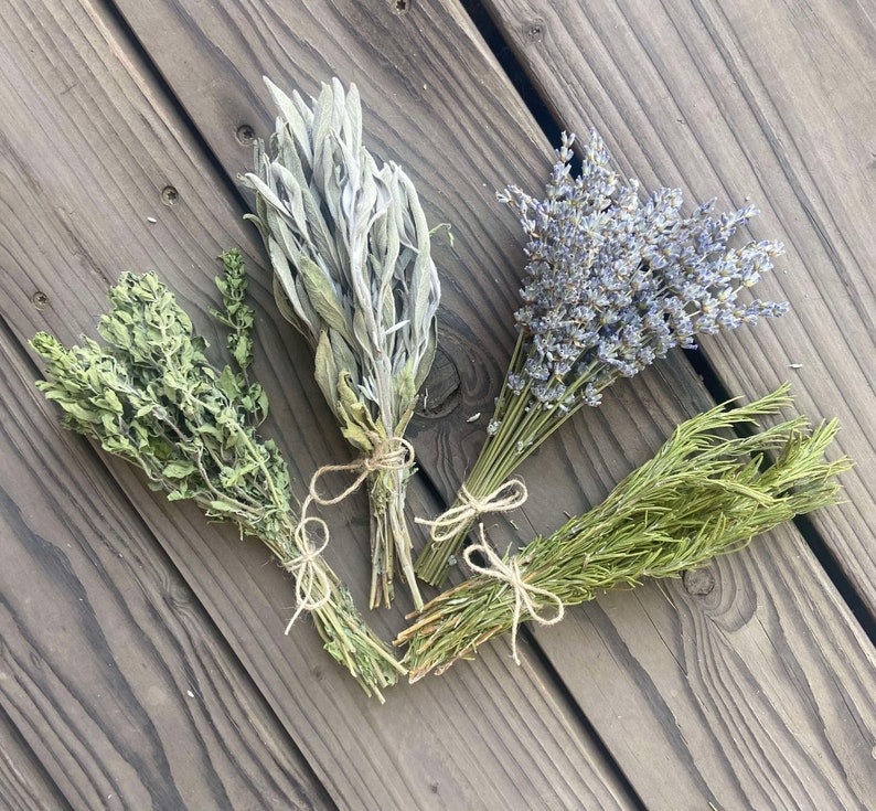 May include: Four bundles of dried herbs, including thyme, sage, lavender, and rosemary, are arranged on a weathered wooden surface. Each bundle is tied with twine, showcasing the natural textures and colors of the herbs.