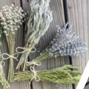 May include: Several dried flower bouquets tied with twine, arranged on a wooden surface. The bouquets include varieties of white, gray, and lavender flowers, and green foliage. The natural tones of the flowers contrast with the wood.