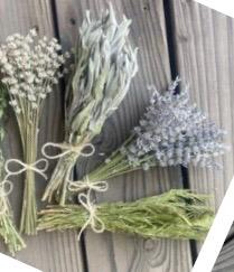 May include: Several dried flower bouquets tied with twine, arranged on a wooden surface. The bouquets include varieties of white, gray, and lavender flowers, and green foliage. The natural tones of the flowers contrast with the wood.