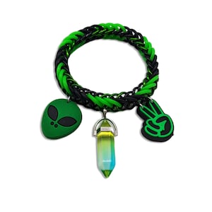 May include: A black and green rubber bracelet with three charms: an alien head, a peace sign, and a crystal-shaped charm.