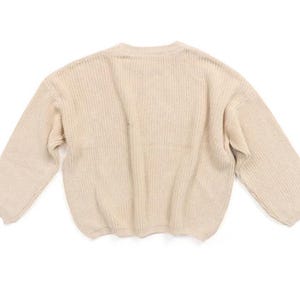 May include: A cream-colored knitted sweater with long sleeves and a ribbed texture.