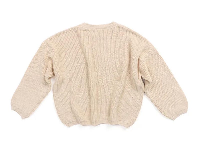 May include: A cream-colored knitted sweater with long sleeves and a ribbed texture.