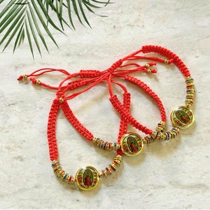May include: Three red woven bracelets with gold accents and a central medallion featuring a religious image. The bracelets have adjustable cords and are adorned with colorful beads.
