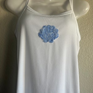 May include: White ribbed tank top with a blue and white seashell design on the front.