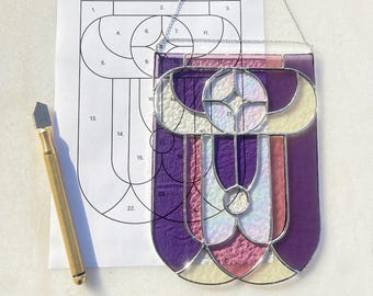 May include: A stained glass project in progress, featuring a purple, pink, and white design with a silver frame. The glass pieces are numbered and a pattern is visible in the background.