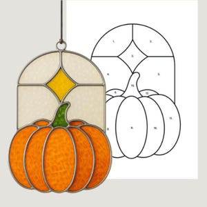 May include: Stained glass pumpkin with a green stem and orange body, suspended from a metal ring. The pumpkin is set against a cream-coloured background with a yellow diamond. A black and white pumpkin pattern is to the right.