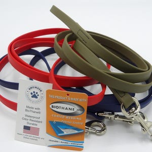 May include: A collection of dog leashes in red, blue, and olive green. The leashes are made of a durable, waterproof material. Two tags are visible, one with the brand name and the other with the material information.