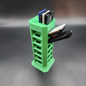 May include: A green plastic storage tower with multiple slots for holding memory cards and other small electronics. The tower has a hexagonal base and is about 10 inches tall.