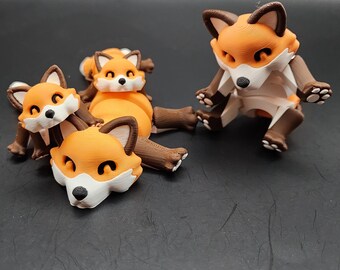 May include: A collection of orange, white, and brown fox figurines. The foxes have detailed features, including pointed ears, black noses, and expressive eyes. One fox is standing, while the others are lying down. The figurines are likely 3D-printed.