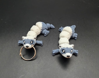 May include: Two gray and white ferret figurines with black eyes. One ferret has a gold ring attached to its body.