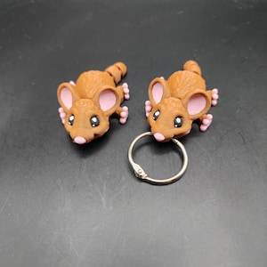 May include: Two brown mouse-shaped keychains with pink ears and black eyes. The keychains are attached to a silver key ring.