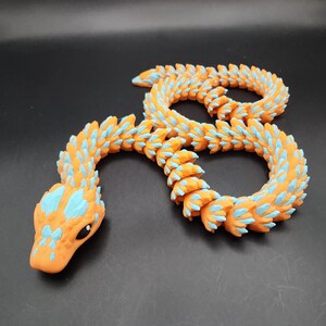 May include: Orange and blue segmented snake toy with a spiky texture. The snake is curled into a circle shape.