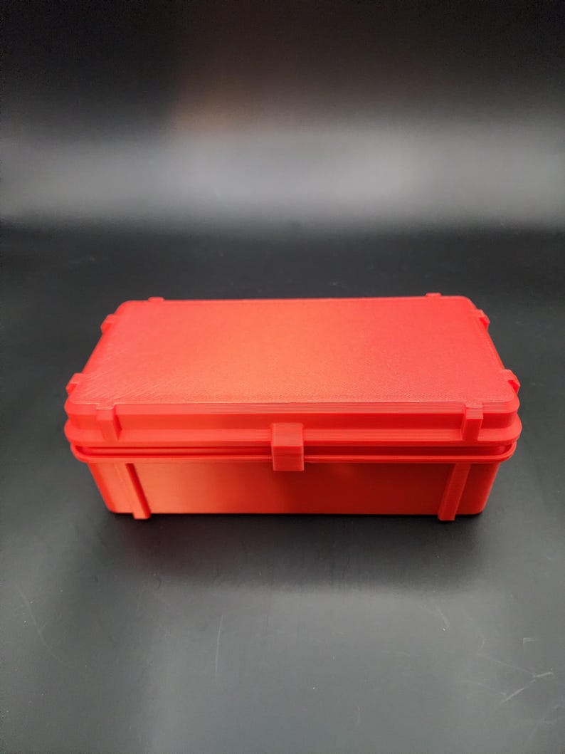 Puede incluir: Una caja de almacenamiento de pl&aacute;stico roja con una tapa con bisagras. La caja es rectangular y tiene una superficie lisa.