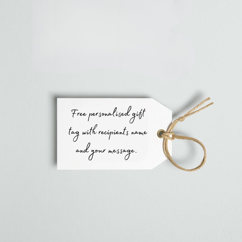 Może przedstawiać: Biała etykieta prezentowa z napisem "Free personalised gift tag with recipient's name and your message" czcionką w kolorze czarnym. Brązowy sznurek jest przełożony przez złoty otw&oacute;r u g&oacute;ry etykiety.