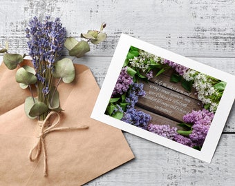 May include: A greeting card with a floral design featuring purple and white lilac blossoms arranged around a wooden background. The text on the card reads: "As the wheel turns and spring's magic awakens, may your stara be filled with abundant blessings and renewed enchantment."