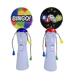 May include: Two white plastic handheld bingo game toys with spinning colorful wheels. One wheel has a black background with the word "BINGO" in colorful letters. The other wheel has a rainbow background with the word "BINGO!" in white letters.