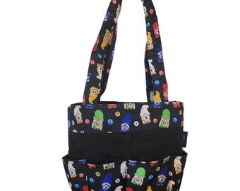 Può includere: Una borsa tote nera con un motivo ripetuto di gnomi colorati e palline da bingo. La borsa presenta due tracolle, una fascia orizzontale nera a tinta unita al centro e tre tasche esterne lungo il bordo inferiore della borsa.