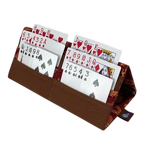 Pu&ograve; includere: Un porta carte marrone con fodera fantasia rossa, contenente diversi mazzi di carte da gioco. Le carte mostrano diversi semi e numeri. Il porta carte ha un design semplice ed &egrave; realizzato in tessuto.