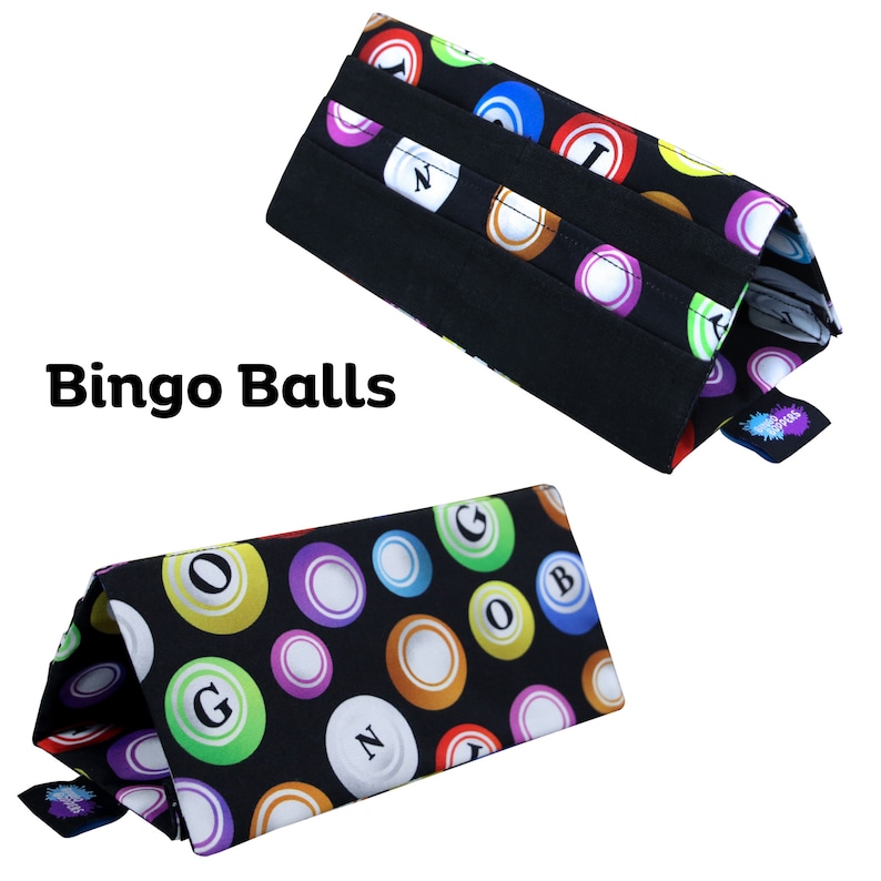 Pu&ograve; includere: Due porta-biglie da bingo in tessuto nero con un motivo colorato di biglie da bingo. I porta-biglie sono di forma triangolare e presentano la scritta "Bingo Balls". Le biglie da bingo sono di vari colori, tra cui rosso, verde e viola.