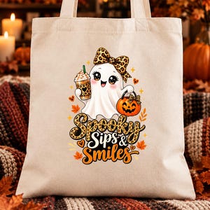 Peut inclure: Un sac fourre-tout en toile beige orné d'un motif représentant un fantôme blanc avec un nœud à imprimé léopard, tenant une tasse à café léopard et un seau citrouille. Le texte "Spooky Sips & Smiles" est imprimé en noir et orange.