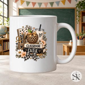 Peut inclure: Un mug en céramique blanche orné d'un motif coloré de fournitures scolaires, incluant une pomme à motif léopard, un gobelet, des crayons, des ciseaux et des livres marqués Classroom Cutie, avec des fleurs et un nœud à carreaux.