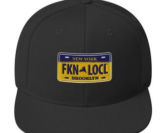 May include: Black and yellow embroidered baseball cap with a New York license plate design that says "FKNLCL" and "BROOKLYN".