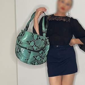 Può includere: Una donna indossa una blusa nera con un colletto in pizzo e una gonna di jeans blu scuro. Tiene in mano una borsa di pelle di serpente verde.