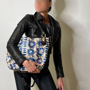 May include: A black leather jacket with a blue, white and brown patterned tote bag. The bag has a gold zipper and a gold buckle.
