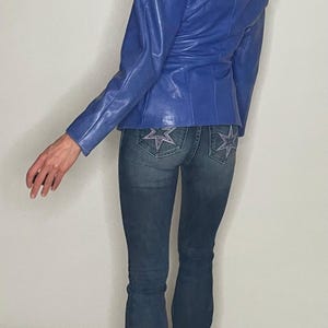 May include: A woman wearing a blue leather jacket and blue denim jeans with star embellishments on the back pockets.