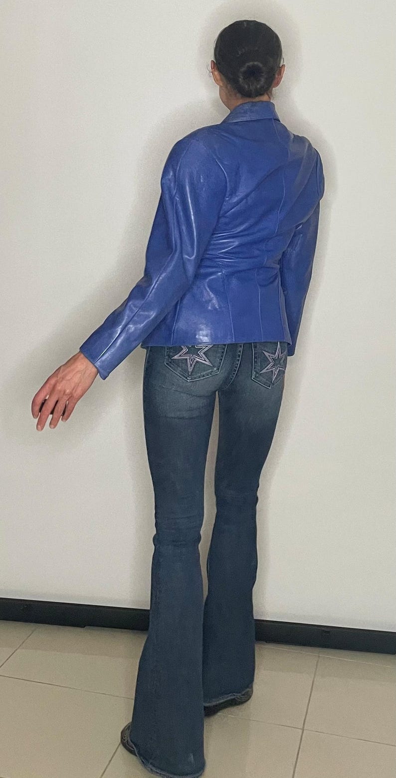 May include: A woman wearing a blue leather jacket and blue denim jeans with star embellishments on the back pockets.