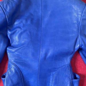 May include: A bright blue leather jacket with a classic design. The jacket has a smooth, shiny finish and a tailored fit.