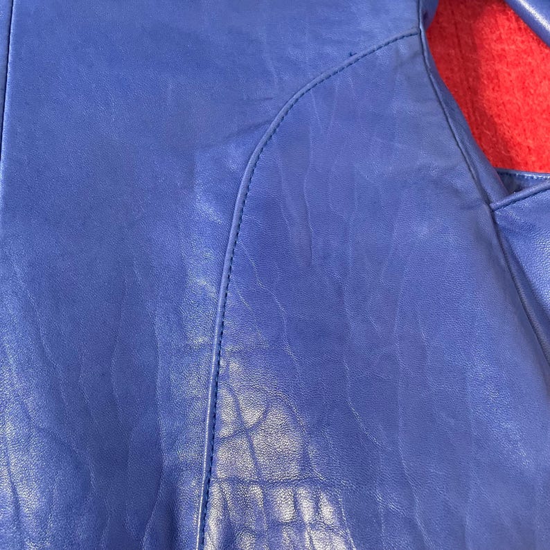 May include: Close-up of a blue leather material with a textured surface and a stitched seam.