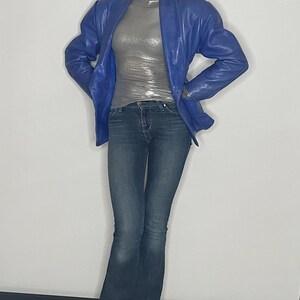May include: A woman wearing a blue leather jacket, a silver sparkly top, blue jeans, and black shoes.