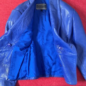 May include: A blue leather jacket with a button closure. The label inside reads "Michael Cohen North Beach Leather".