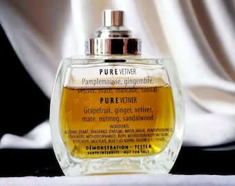 May include: A clear glass bottle of Pure Vetiver fragrance with a silver cap. The bottle is filled with a golden liquid. The label lists the fragrance notes: Pamplemousse, gingembre, vétiver, maté, muscade, santal.  The label also lists the fragrance notes: Grapefruit, ginger, vetiver, maté, nutmeg, sandalwood. The label also includes the ingredients and states that it is a demonstration tester, not for sale.