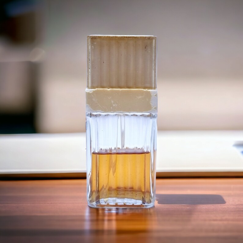 May include: A clear glass bottle with a brown liquid inside. The bottle has a white plastic cap and a textured glass body.